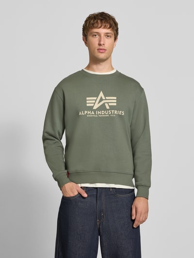 Männermodel trägt Regular Fit Sweatshirt aus Baumwoll-Mix mit Logo-Print von Alpha Industries, grün, Struktur glatt, Ganzkörperansicht von vorne. Kontext: Herren Sweatshirt, gerippte Blende und Abschlüsse, Rundhalsausschnitt, Rückenlänge 67 cm, Ärmellänge 64 cm.