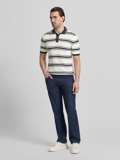 Männermodel trägt Slim Fit Poloshirt in Strick-Optik von MCNEAL, reine Baumwolle, weiß mit dunkelblauen Streifen, Ganzkörperansicht von vorne.