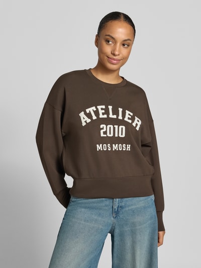 Frauenmodel trägt Oversized Sweatshirt aus Viskose-Mix Modell 'Nima' von MOS MOSH in Braun mit Schriftzug-Patch, Nahaufnahme Oberkörper.