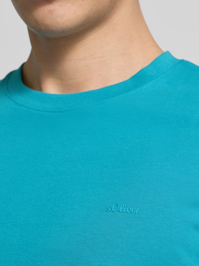 Männermodel trägt Regular Fit T-Shirt aus reiner Baumwolle von s.Oliver RED LABEL in Unifarbe Türkis, Label-Schriftzug, Nahaufnahme Oberkörper.