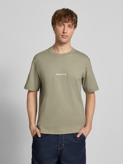 Männermodel trägt T-Shirt mit Label-Stitching Modell 'NORREBRO' von Jack & Jones in Olivgrün aus Baumwolle, Ganzkörperansicht von vorne.