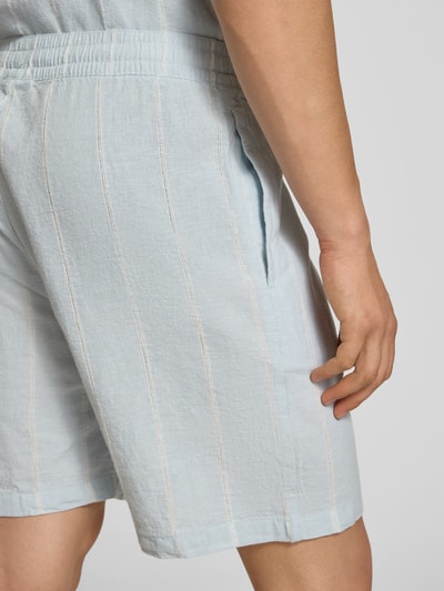 Männermodel trägt Leinenshorts mit Logo-Stitching von REVIEW, hellblauer Baumwoll-Mix mit Leinen-Anteil, Nahaufnahme Oberschenkel.