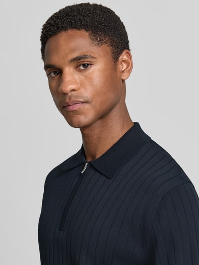 Männermodel trägt Regular Fit Poloshirt mit kurzem Reißverschluss von Drykorn aus Reine Baumwolle, dunkle Farbe, Nahaufnahme Oberkörper. Modell 'NIIVAN', Rückenlänge 68 cm bei Größe M.