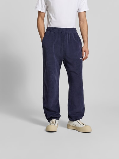 Männermodel trägt Sweatpants aus reiner Baumwolle von RHUDE in Dunkelblau, Frottee, lockere Passform, elastischer Bund, Ganzkörperansicht von vorne.