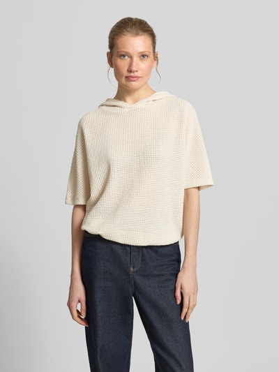 Frauenmodel trägt Strickshirt mit Kapuze Modell 'Gikaria' von OPUS, Material-Mix mit Baumwoll-Anteil, Relaxed-Fit, Strukturmuster, cremefarbene Textur, Rückenlänge 56 cm, Ärmellänge 26 cm, Ganzkörperansicht von vorne.