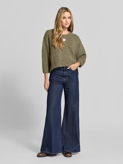 Frauenmodel trägt Oversized Pullover mit Alpaka-Anteil Modell 'East' von American Vintage in Strick-Optik, olivgrün, Ganzkörperansicht von vorne.