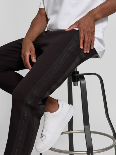 Männermodel trägt schwarze Sweatpants mit Bordüre von Armani Exchange, Label-Print, Baumwoll-Mix, Nahaufnahme Unterkörper, KI-modifiziertes Bild.