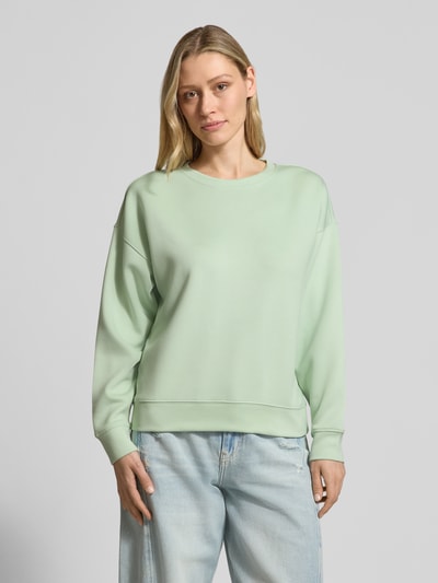 Modelka nosi Sweatshirt aus Viskose-Mix Modell 'Ima' od MSCH Copenhagen, kolor jasnozielony, krój relaxed fit, damska bluza, widok całej sylwetki z przodu.