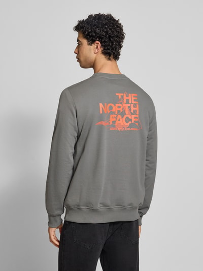 Mężczyzna nosi bluzę Sweatshirt mit Label-Print od The North Face z bawełny, krój regular fit, prążkowane wykończenia, okrągły dekolt, nadruk z logo na plecach. Ganzkörperansicht Rückansicht.