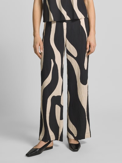 Frauenmodel trägt Stoffhose aus Viskose-Mix im Allover-Look Modell 'NIKITA' von Mango, Relaxed-Fit, beige-schwarz gemustert, Nahaufnahme Unterkörper, Bundweite bei Größe 36: 41 cm, Innenbeinlänge: 77 cm.