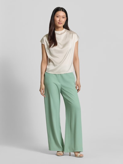 Modelka kobieca nosi spodnie materiałowe 'Stoffhose mit elastischem Bund und Eingrifftaschen' od Jake*s Collection, mieszanka materiałów z dodatkiem streczu, krój wide fit, elastyczny pas, wpuszczane kieszenie, tył z imitacją kieszeni z wypustką, szerokość w rozmiarze 36: 38 cm, długość wewnętrzna nogawki w rozmiarze 36: 78 cm, pastelowa zieleń, gładka faktura, pełny widok sylwetki z przodu.