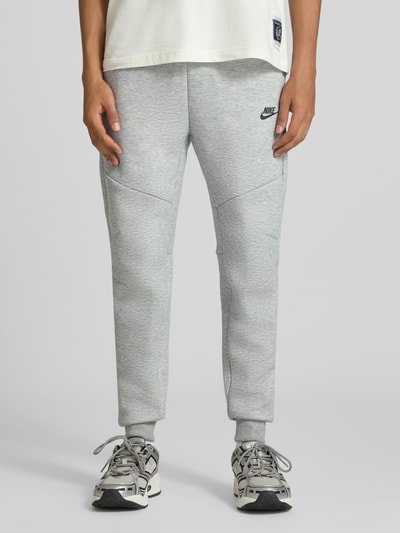 Männermodel trägt Slim Fit Sweathose aus Baumwoll-Mix von Nike in Hellgrau mit melierter Textur, Ganzkörperansicht von vorne. Herren Sweathose von Nike.