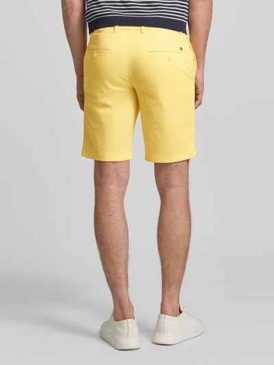 Mężczyzna nosi Regular Fit Bermudas aus Baumwoll-Mix od Tommy Hilfiger, żółty kolor, kieszenie, logo, bawełniany materiał, widok z tyłu całej sylwetki.