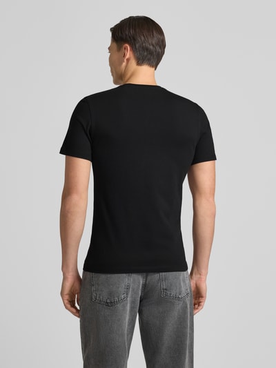 Männermodel trägt T-Shirt mit Label-Detail von Guess in Schwarz, Baumwoll-Elasthan-Mix, Regular Fit, Ganzkörperansicht Rückansicht.