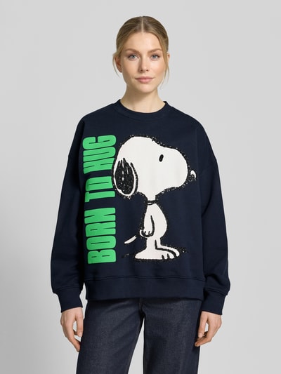 Frauenmodel trägt Loose Fit Sweatshirt aus reiner Baumwolle Modell 'JUMBRELLA EMBO' von Essentiel Antwerp in Dunkelblau mit Snoopy Motiv-Print, grüner Schrift, Pailletten und Perlen, überschnittenen Schultern, Rundhalsausschnitt und gerippten Abschlüssen, Sweat-Material; Ganzkörperansicht von vorne.