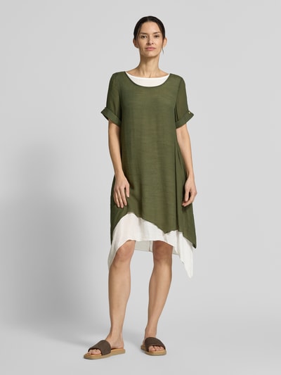 Frauenmodel trägt Knielanges Kleid aus Viskose-Mix von Apricot in Olivgrün und Weiß, gerader Schnitt, asymmetrische Form, Rundhalsausschnitt, knielang, Ärmel mit Aufschlag, Ganzkörperansicht von vorne.
