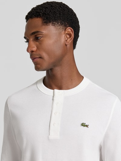 Männermodel trägt Regular Fit Langarmshirt aus reiner Baumwolle von Lacoste in Weiß, gerippte Textur, Nahaufnahme Oberkörper, Herren Langarmshirt von Lacoste.
