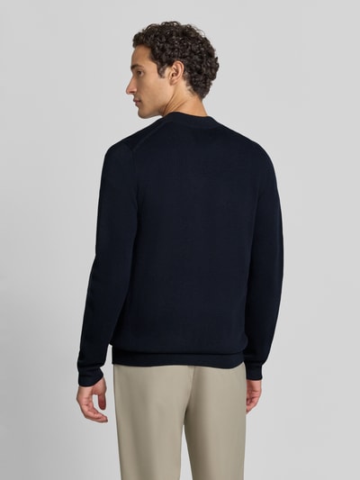 Männermodel trägt Slim Fit Strickjacke aus Baumwoll-Mix mit Stehkragen von Christian Berg Men, dunkelblau, gerippte Abschlüsse, Ganzkörperansicht Rückansicht.