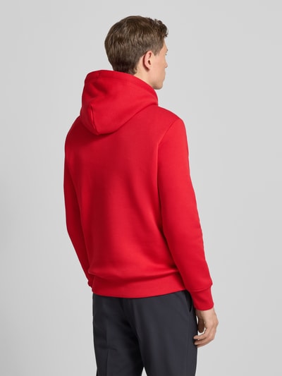Męski model nosi Hoodie mit Label-Stitching und Känguru-Tasche od Gant, czerwony kolor, bawełniany miks, regular fit, całkowity widok z tyłu.