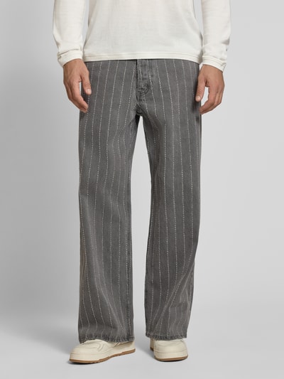 Mannermodel draagt Wide Fit Jeans aus reiner Baumwolle van Wood Wood, grijze kleur met witte verticale strepen, 5-pocketmodel, puur katoen, knoop- en ritssluiting, heren jeans, vooraanzicht volledige lengte.