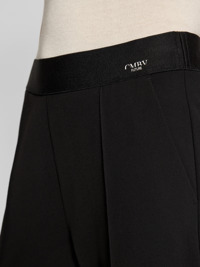 Frauenmodel trägt Straight Fit Stoffhose mit Ziernaht Modell 'Cameron' von Cambio, elastischer Bund, Nahaufnahme Oberkörper, schwarze Farbe, glatte Textur, Logo-Print, Gesäßtaschen, verkürzte Passform.