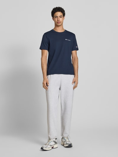 Männermodel trägt T-Shirt mit Label-Stitchings und Rundhalsausschnitt von CHAMPION in Dunkelblau, Reine Baumwolle, Regular-Fit, Ganzkörperansicht von vorne. Rückenlänge bei Größe M: 69 cm.