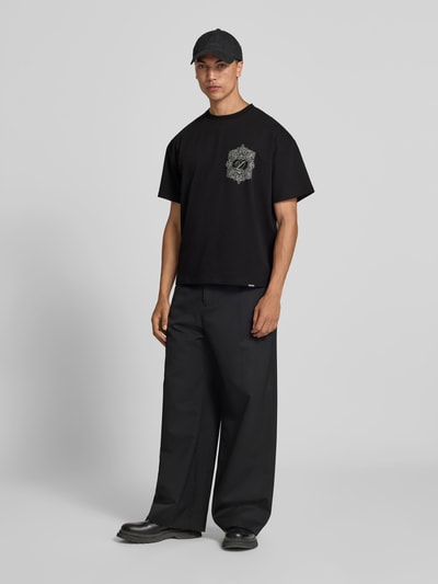 Männermodel trägt Regular Fit T-Shirt aus Baumwoll-Mix von Don't Waste Culture, schwarzes Unifarbenes-Design mit Label-Detail, Ganzkörperansicht von vorne.