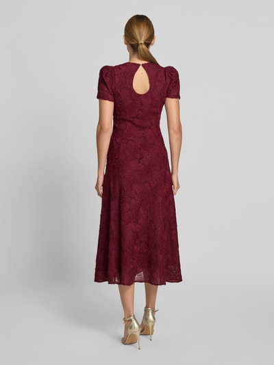 Frauenmodel trägt Maxikleid mit floralem Allover-Besatz von ROTATE aus Elastischer-Material-Mix in Bordeaux, taillierte Passform, Rückansicht, Ganzkörperansicht Rückansicht, Kurzärmelig, mit Rundhalsausschnitt, Kontext: Gesamtlänge 133 cm, Brustweite 45 cm, Ärmellänge 22 cm.
