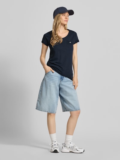 Frauenmodel trägt Damen T-Shirt mit Brusttasche Modell 'GS23' von G.I.G.A. DX, Reine Baumwolle, Regular-Fit, V-Ausschnitt, dunkelblau, kombiniert mit hellblauer Shorts, Ganzkörperansicht von vorne. Rückenlänge bei Größe 36: 64 cm.