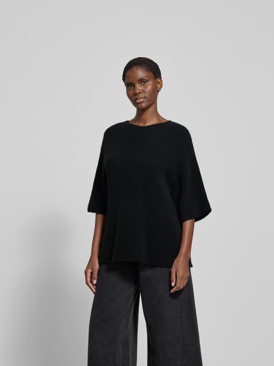 Frauenmodel trägt Pullover mit 3/4-Ärmel von black palms, Alpaka-Mix mit Woll-Anteil, lockerer Schnitt, Rundhalsausschnitt, Rückenlänge bei Größe S 62 cm, einfarbig schwarz, weiche Textur, Ganzkörperansicht von vorne.