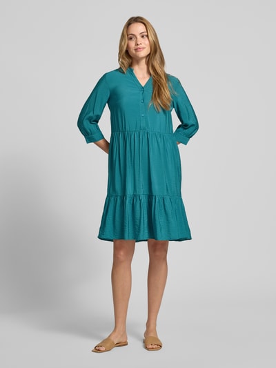Frauenmodel trägt Relaxed Fit Midikleid aus Viskose-Mix mit Tunika-Ausschnitt von Christian Berg Woman, Knopfleiste, Halbarm, Ganzkörperansicht von vorne. Rückenlänge bei Größe 36: 106 cm, Brustweite bei Größe 36: 45 cm, Ärmellänge bei Größe 36: 44 cm. Das Kleid zeigt glatte, strukturierte Textur in kräftigem Türkis und lockerer Silhouette.