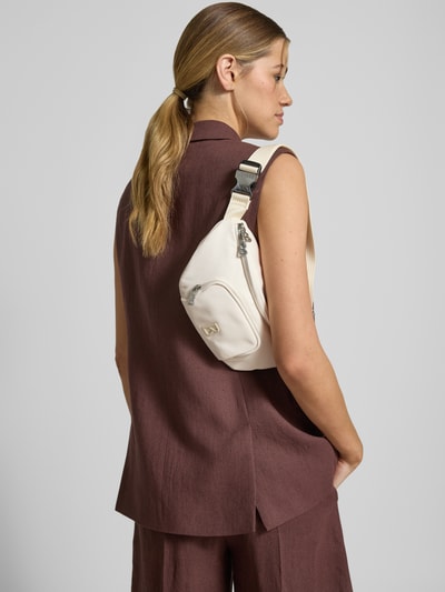 Frauenmodel trägt Handtasche mit Label-Detail Modell 'verbier play 1.0 janica' von BOGNER in Creme, verstellbarer Schulterriemen, Ganzkörperansicht Rückansicht. Hauptfach mit Zweiwege-Reißverschluss, Maße: Breite 28 cm, Länge 16 cm, Tiefe 4 cm, Schulterriemen Länge 72 cm.