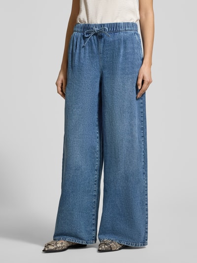 Frauenmodel trägt Wide Leg Jeans aus Baumwoll-Viskose-Mix Modell 'VALERIA' von Vero Moda in Denim-Optik mit Wide Leg Passform, Tunnelzug, elastischem Bundabschluss, seitlichen Eingrifftaschen und angedeuteten Gesäßtaschen; mittleres Blau, strukturierte Oberfläche, Ganzkörperansicht von vorne.