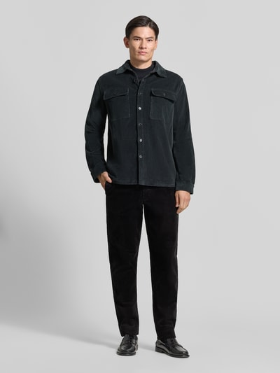 Männermodel trägt schwarze Tapered Fit Cordhose aus reiner Baumwolle Modell 'LEROY' von Selected, Ganzkörperansicht von vorne. Herren Cordhose.
