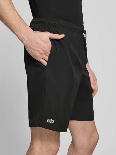 Männermodel trägt Relaxed Fit Sport-Shorts mit Logo-Stitching von Lacoste Sport, unifarben schwarz, seitliche Eingrifftaschen, Nahaufnahme Oberschenkel.