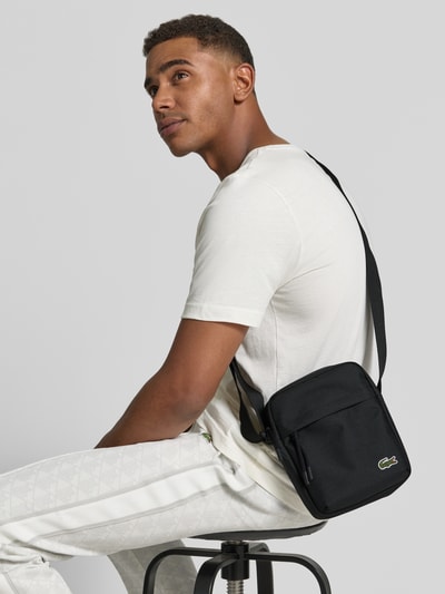 Männermodel trägt schwarze Umhängetasche mit Logo-Detail Modell 'NEOCROC' von Lacoste, Herren Umhängetasche, Nahaufnahme Oberkörper.