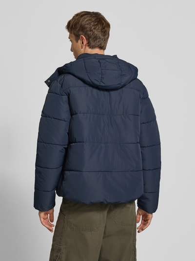 Männermodel trägt Steppjacke mit Kapuze und Reißverschluss von Superdry in Dunkelblau, glatte wattierte Oberfläche, Ganzkörperansicht Rückansicht. Rückenlänge 71 cm, Schulterbreite 50 cm, Brustweite 56 cm, Ärmellänge 83 cm, Regular Fit.