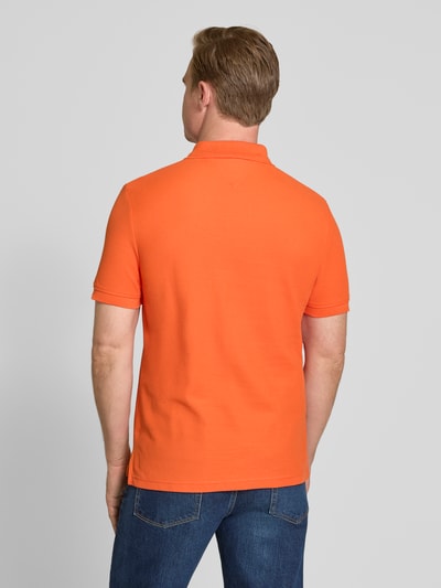 Męski model nosi Regular Fit Poloshirt aus reiner Baumwolle od Tommy Hilfiger, pomarańczowy, jednokolorowy, pikowany materiał, widok całej sylwetki z tyłu.