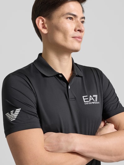 Männermodel trägt Regular Fit Poloshirt mit Logo von EA7 Emporio Armani, schwarzer Material-Mix mit Stretch-Anteil, Nahaufnahme Oberkörper.