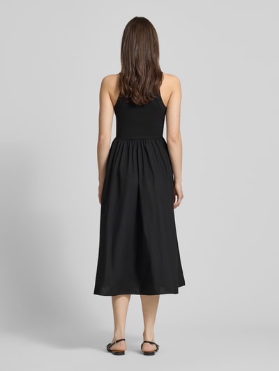 Frauenmodel trägt Midikleid aus reiner Baumwolle von Tommy Jeans in Schwarz, ärmellos, A-Linie, einfarbig, Ganzkörperansicht Rückansicht.