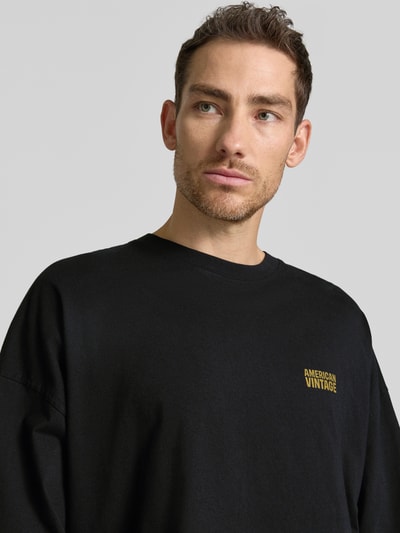 Männermodel trägt Longsleeve mit Logo-Print Modell 'GIXY' von American Vintage aus Reine Baumwolle in Schwarz, Nahaufnahme Oberkörper. Loose-Fit, Rundhalsausschnitt, Rückenlänge 72 cm bei Größe M/L.