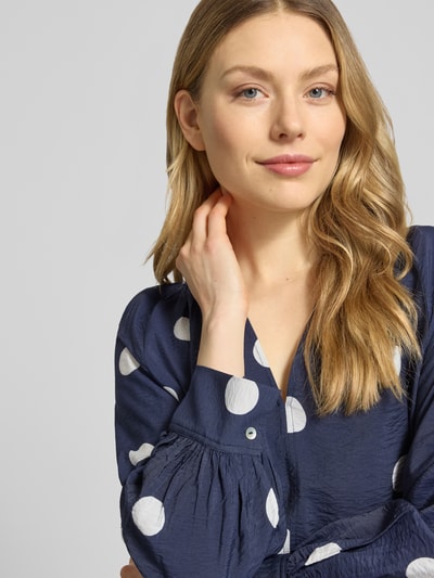 Frauenmodel trägt Bluse aus Viskose-Mix mit Serafino-Ausschnitt von Christian Berg Woman, dunkelblau mit weißen Punkten, Nahaufnahme Oberkörper. Loose-Fit, verlängerter Rücken, Rückenlänge bei Größe 36: 61 cm, Ärmellänge 60 cm.