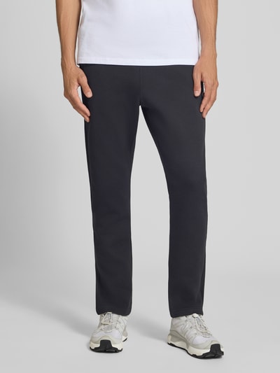 Männermodel trägt Sweatanzug mit Label-Details von Champion, mieszanka bawełny, prosty krój, elastyczny pas, wpuszczane kieszenie, czarny, Ganzkörperansicht von vorne. Szerokość w rozmiarze M: 76 cm, Długość tyłu w rozmiarze M: 70 cm, Szerokość ramion w rozmiarze M: 51 cm, Długość rękawów w rozmiarze M: 69 cm, Długość wewnętrzna nogawki w rozmiarze M: 76 cm.