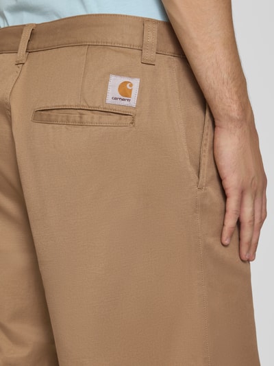 Männermodel trägt Bermudas mit Baumwoll-Anteil Modell 'Brader' von Carhartt Work In Progress in Beige, Eingriff- und Gesäßtaschen, Nahaufnahme Oberkörper. Material-Mix, Relaxed Fit, Knopf- und Reißverschluss, Gürtelschlaufen, Bundweite 44 cm, Innenbeinlänge 30 cm.