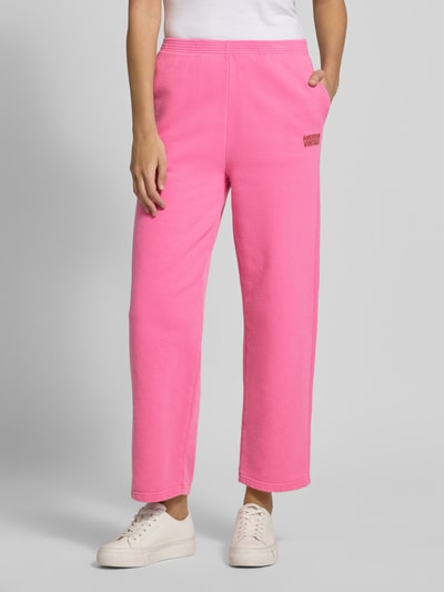 Vrouwenmodel draagt felroze Sweatpants met Labelprint Model 'PLIZZY' van American Vintage, puur katoen, relaxed fit, elastische band, binnenbeenlengte maat S 71 cm, voorkant volledige lichaamsweergave.