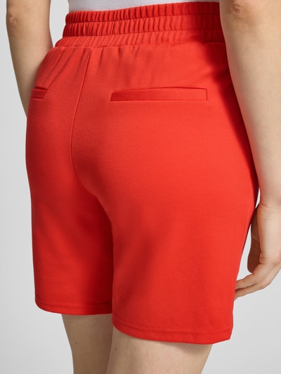 Vrouwenmodel draagt shorts met elastische band model Kate van ICHI, materiaalmix met viscose, regular fit, binnenbeenlengte 18 cm, bandwijdte maat S 39 cm, felrode kleur, gladde textuur, detailopname achterkant.