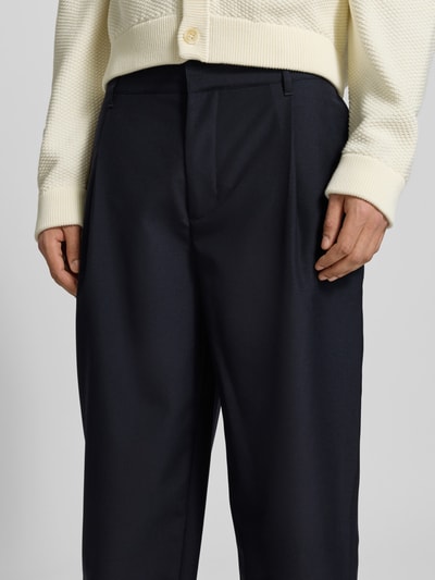 Männermodel trägt Straight Fit Stoffhose mit Bundfalten von MAISON KITSUNÉ, Reine Baumwolle, dunkle Farbe, Nahaufnahme Oberkörper. Innenbeinlänge 63 cm, Bundweite 44 cm, Haken- und Reißverschluss, verkürzte Passform.