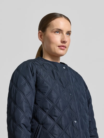 Kobieta nosi Regular Fit kurtkę z efektem pikowania z kapturem model 'Fenya' od Soyaconcept, wpuszczane kieszenie, listwa guzikowa, długość tyłu w rozmiarze S: 65 cm, szerokość ramion w rozmiarze S: 40 cm, szerokość klatki piersiowej w rozmiarze S: 54 cm, długość rękawów w rozmiarze S: 65 cm, ciemnogranatowa, geometryczne pikowanie, zbliżenie na górną część tułowia