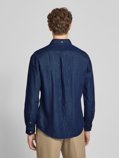 Männermodel trägt Slim Fit Jeanshemd aus reiner bawełna von Barbour w kolorze ciemnego denim, kołnierzyk typu button down, krój slim fit, długi rękaw, wyhaftowane logo, zaokrąglone wykończenie, widok całej sylwetki z tyłu.