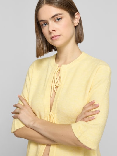 Modelka kobieca nosi Regular Fit Cardigan mit Schnürungen Modell 'SIMONI' od Only, żółty, faktura dzianiny, dekolt okrągły, półrękaw; zbliżenie na górną część ciała